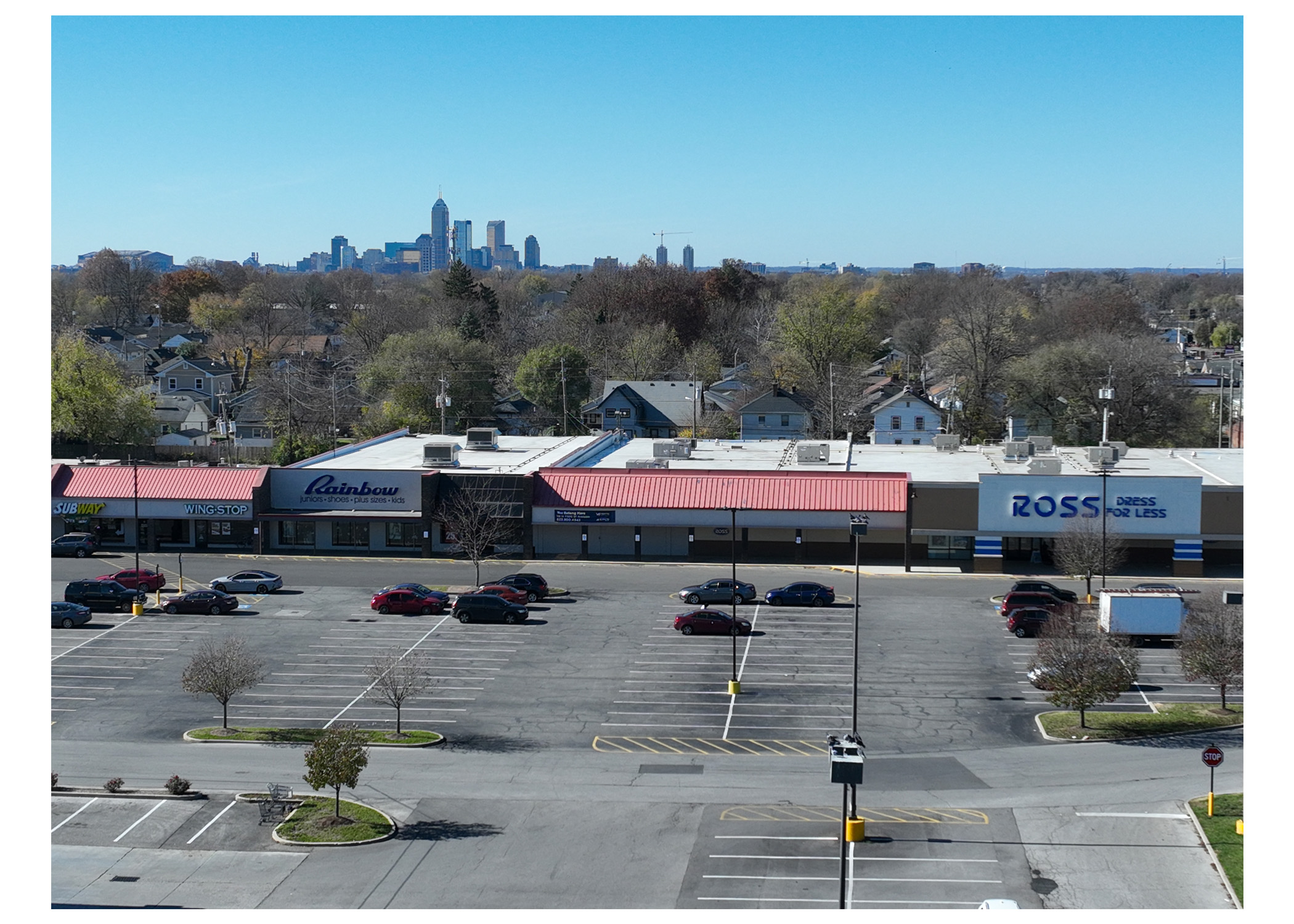 Linwood Square, Subway, Wing Stop, Rainbow, Ross Dress For Less, and parking lot. Aerial view, downtown Indianapolis skyline behind stores.